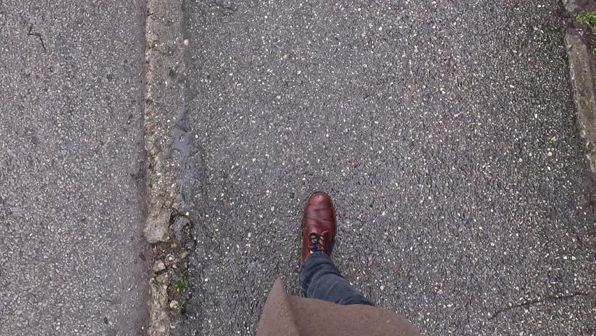 Businessman wearing elegant brown boots and jeans is walking on damaged asphalt road during rainy weather in winter, first person perspective first person pov shot