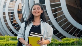 Latina young student smiling at camera wearing blue shirt holding books and notebooks at modern university campus. - Powered by Shutterstock - Get 15% off with code: PIKWIZARD15