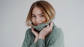 Portrait of a cheerful young woman smiling and holding the collar of her cozy green turtleneck sweater. Perfect for fashion and lifestyle themes. Smiling Young Woman in Cozy Green Sweater - Powered by Shutterstock - Get 15% off with code: PIKWIZARD15