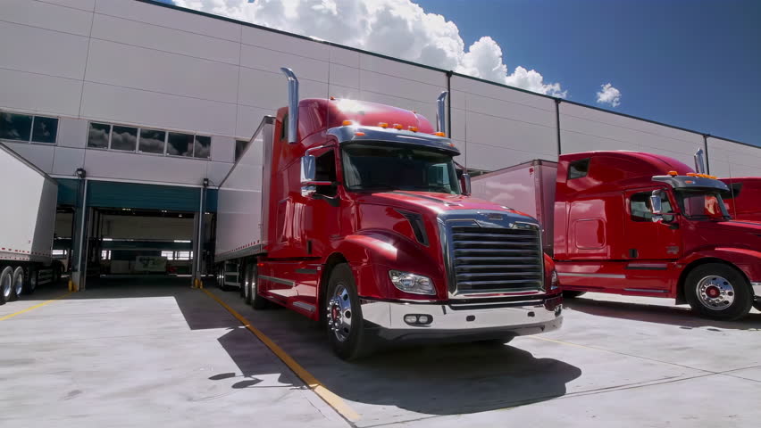 Vibrant red trucks are parked neatly outside a modern distribution facility located under clear blue skies. 3D Illustration