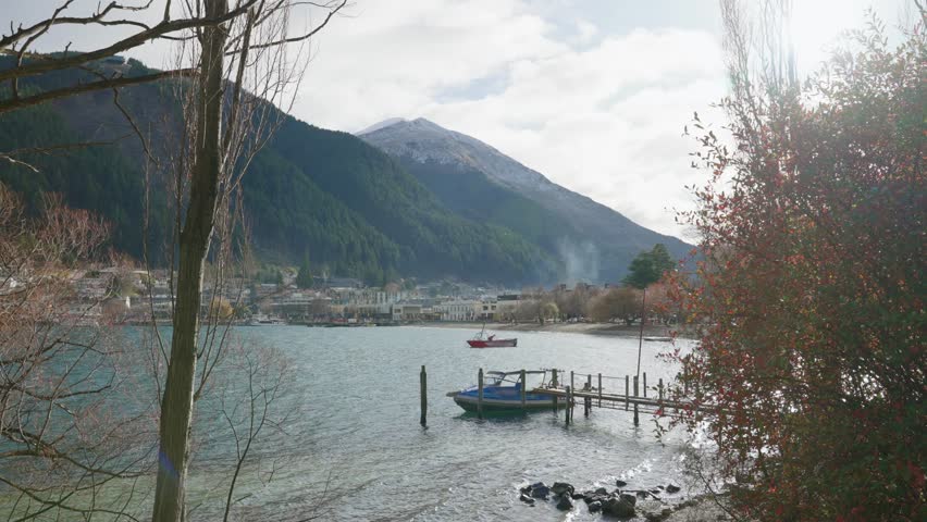 Boats in small marina in Queenstown city in New Zealand on cold autumn day. Small dock with rental and private boats anchored and moored in bay close to famous town center in beautiful South Island