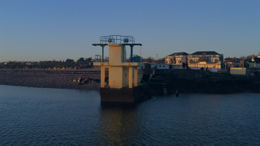 Stunning aerial shot of the iconic Blackrock diving board at sunset, reflecting on the water with warm, pleasant colors