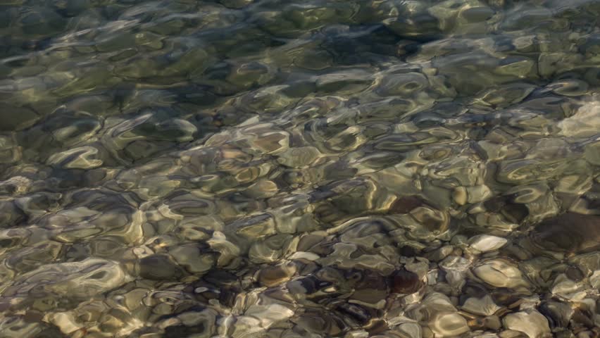 Clear water over smooth pebbles at Lake Garda, Sirmione, Italy, reflecting sunlight with natural pattern