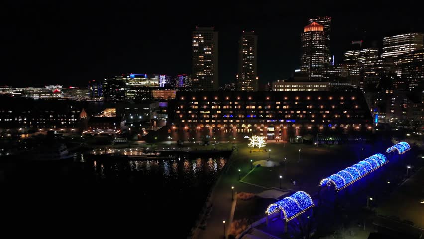 Aerial approaching shot of lighting skyline of Boston Town with Skyscrapers at night. Festive decorated city at channel. Wide shot. Massachusetts, USA.