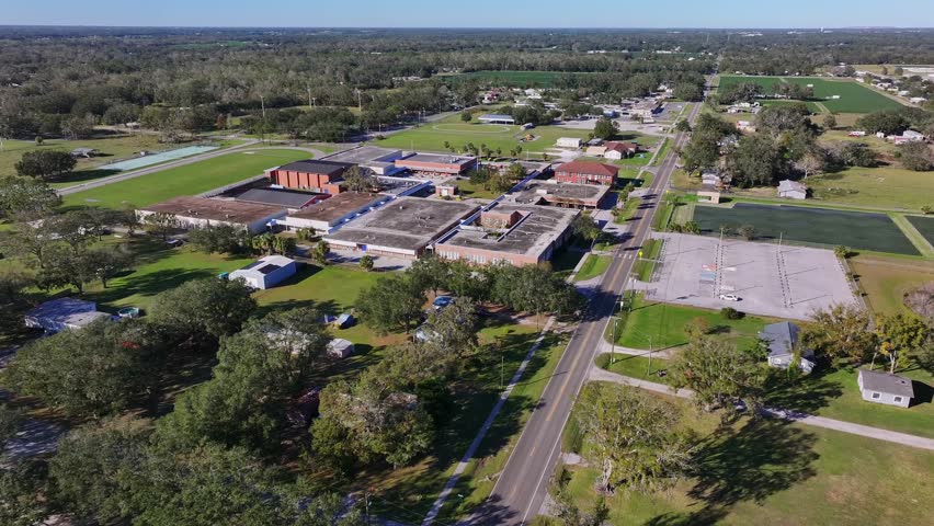 Aerial top down shot of american high school in Plant City, Florida during sunny day. Suburb district with forest trees in distance.