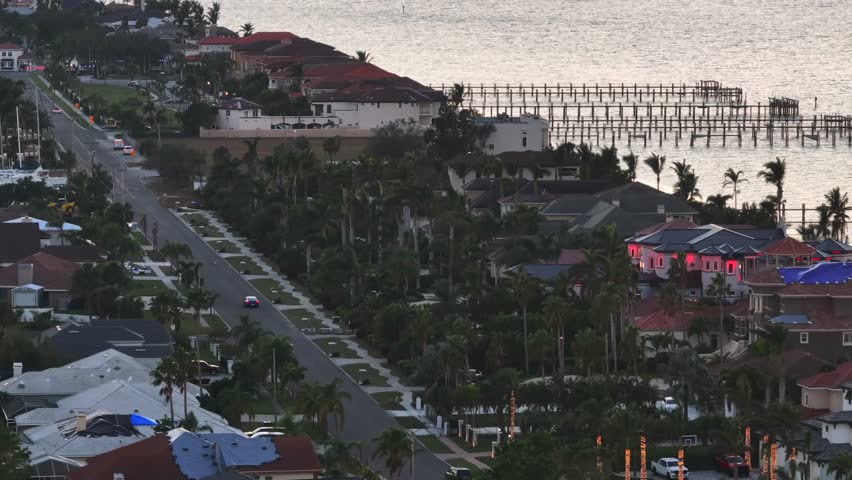Dusk scene with car on street in luxury neighborhood of Florida. Private jetty at villa and bay access. Aerial zoom wide shot.