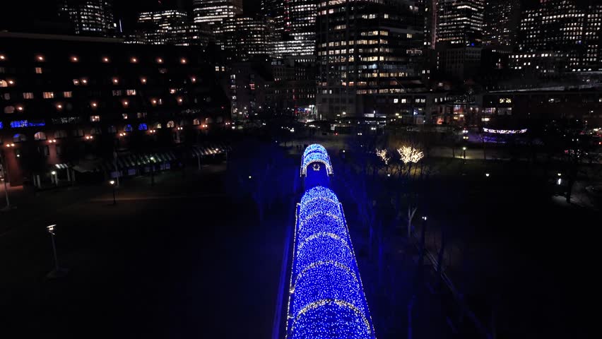 Skyline of Boston at night with lighting skyscraper and High-rise Buildings. Blue lighting bridge at waterfront of City. Aerial tilt up wide shot. Massachusetts, United States.
