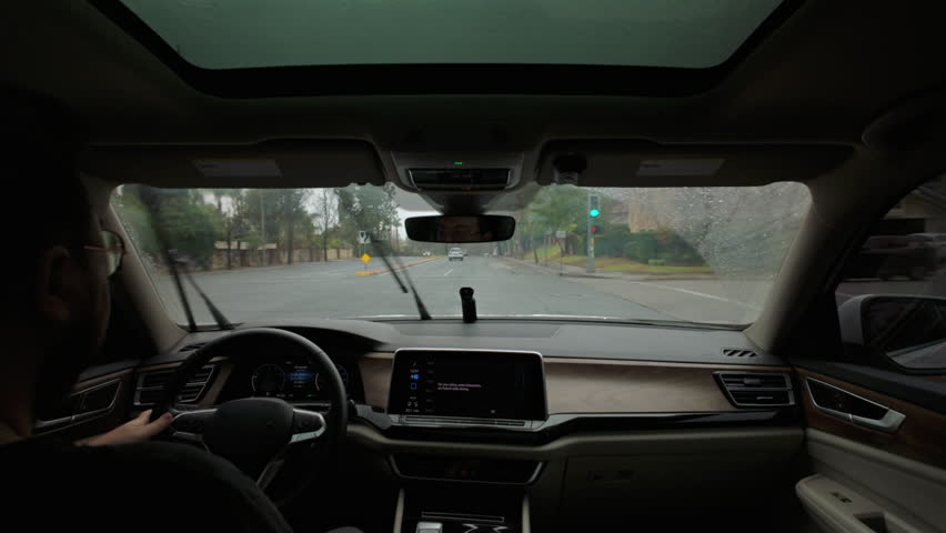 The image shows a modern car with a spacious interior driving smoothly on a rainy highway, as the driver admires the lush greenery outside, creating a serene yet adventurous atmosphere