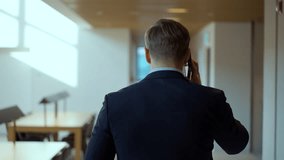 Businessman walking office corridor talking on a mobile phone - rear view tracking shot - Powered by Shutterstock - Get 15% off with code: PIKWIZARD15