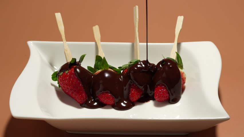 A white plate with four strawberries and chocolate sauce. A plate on the table. Strawberries on a white plate are poured with chocolate.