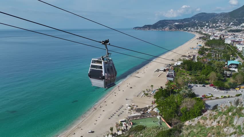 Aerial Video of a Cable Car Gliding Over the Coastline With a White Sand Beach and Crystal-Clear Blue Water Below Funicular above a scenic beach. Aerial footage of a peaceful seaside setting.