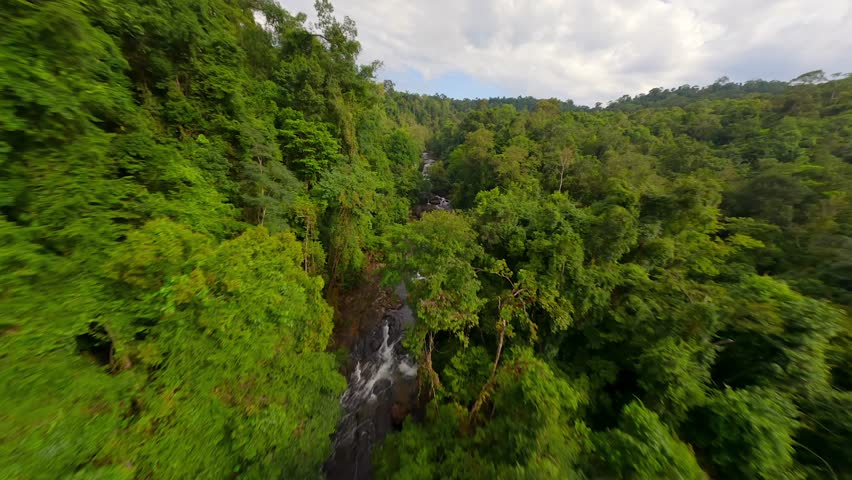 Dynamic FPV flight over the lush jungle with tropical river and waterfall in Thailand