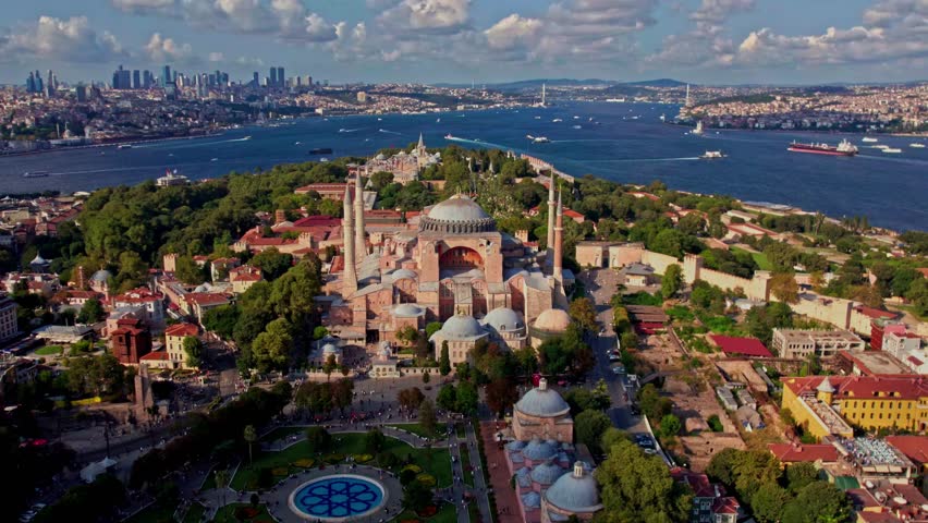 A stunning aerial view of Hagia Sophia in Istanbul, surrounded by lush greenery and the Bosphorus. The city skyline and a partly cloudy sky enhance the scenes beauty.
