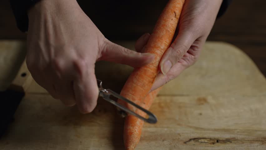 A woman peels a carrot using a vegetable peeler.