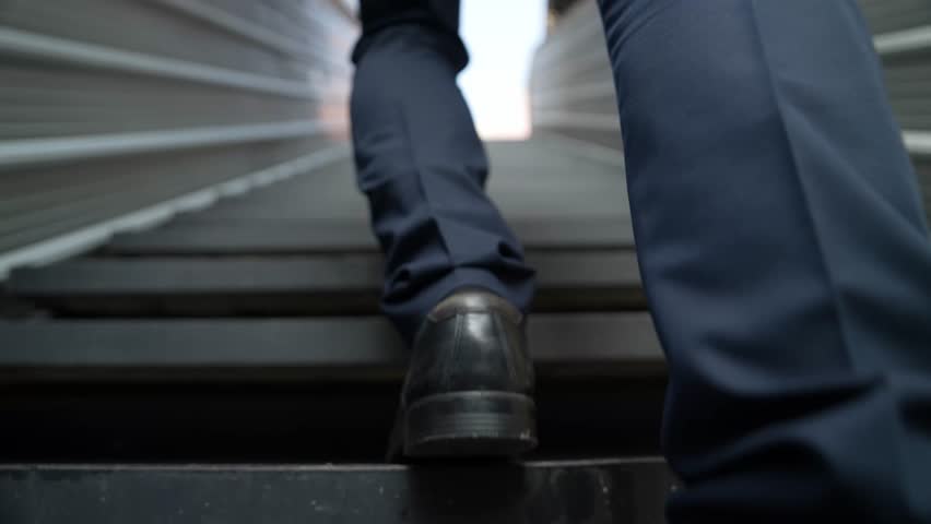 Closeup of successful business man leg walking up to stair. Manager changing workplace, discover a new thing, growth or getting promotion or walking in to light. Rising up. Focus on leg. Exultant.