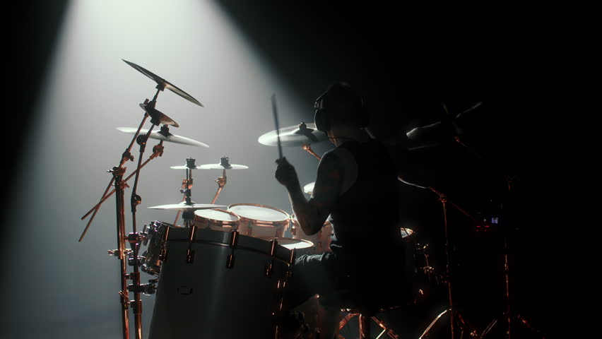 Silhouette of professional drummer on stage in darkness, gig in concert hall. Cinematic backlit view of male musician punching drum set, power of music and rhythm, back view, rock musical performance