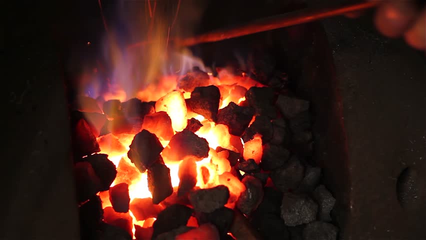 Blacksmith at work. Coal fire melts iron in a furnace for further processing with a hammer on an anvil in smithy, close-up. Traditional manual production in the forge, blacksmith workshop