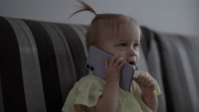 Funny cute child girl holding smartphone to ear, mimicking phone call. Joyful infant in light-colored outfit sitting on couch showcasing curiosity and imagination talking using smartphone at home. - Powered by Shutterstock - Get 15% off with code: PIKWIZARD15