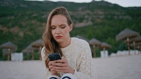 Confused woman watching cellphone sitting evening seashore alone closeup. Frowned lady reading smartphone message at sea vacation. Puzzled attractive girl receiving dissatisfying sms on mobile phone. - Powered by Shutterstock - Get 15% off with code: PIKWIZARD15