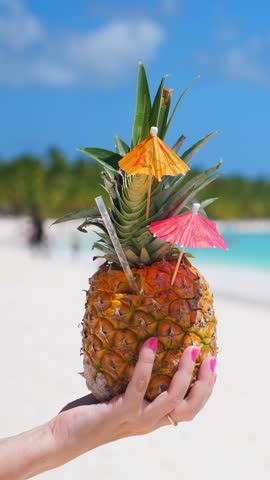 Pineapple cocktail in hand with caribbean beach background. Travel destinations. summer vacation. Vertical footage