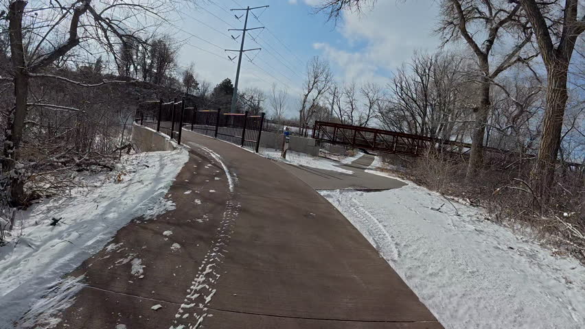 First person POV from bike riding on a biking trail and footbridge across a river on cold winter afternoon in Colorado