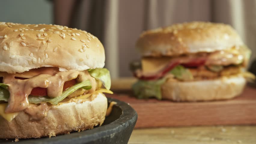 Two mouth-watering, juicy traditional burgers, drizzled with sauce, are served to hungry restaurant visitors who were looking forward to opportunity to enjoy their delicious taste.