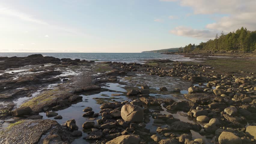 Serene rocky beach coastline with tide pools and gentle waves under a cloudy blue sky at sunset, creating a peaceful atmosphere. British Columbia, Canada.
