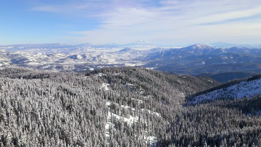 A breathtaking aerial journey from the summit of Mt. Ashland, flying toward the distant peak of Mt. Shasta over a vast, snow-covered winter landscape.