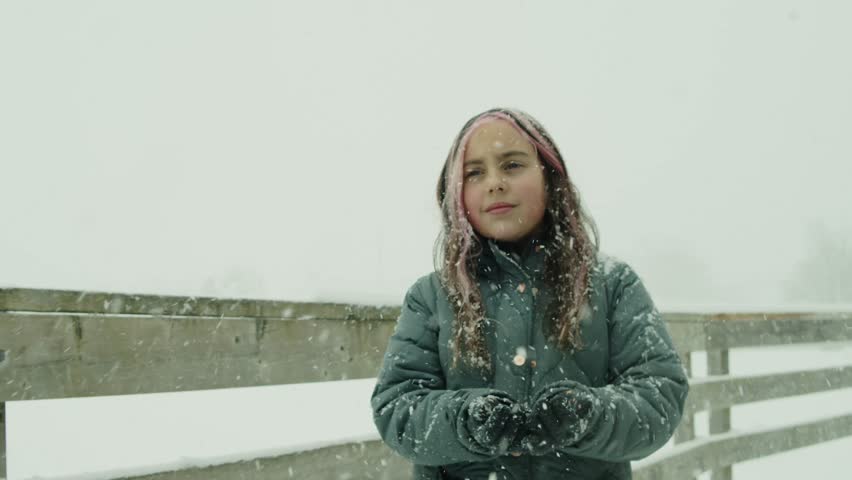 A Nine-Year-Old Girl In Winter Clothes Feels The Snowfall On Her Hand By A Snowy Lake. She Stares At The Sky, Capturing The Serenity Of The Winter Landscape And The Magic Of Snowfall.