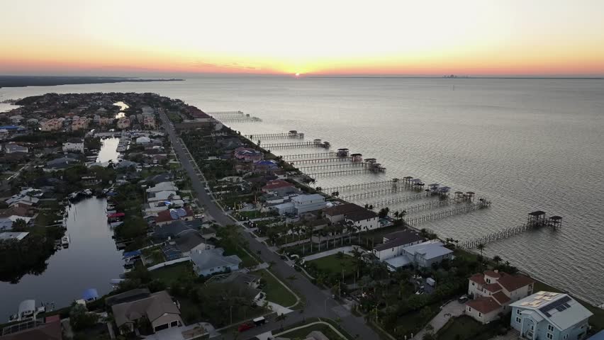 Luxury villas along bay with private jetty boardwalk at Apollo Beach, Florida, USA. Aerial backwards weide shot. Dusk scene with cars on street.