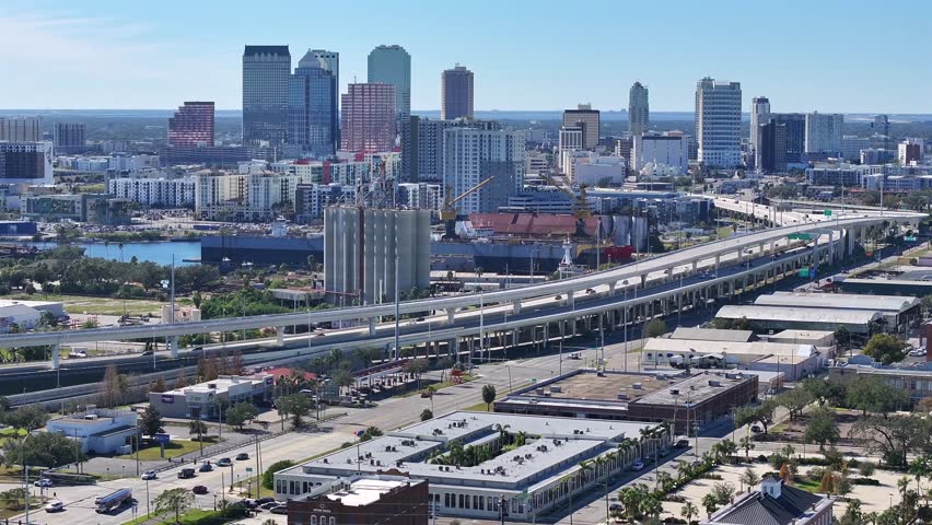 Downtown of Tampa with skyline and working cranes on industrial port. Traffic on highway during sunny day in Florida. Aerial establishing wide shot. Housing area in suburb.