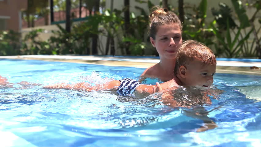 Happy mother teaching to swim daughter in swimming pool