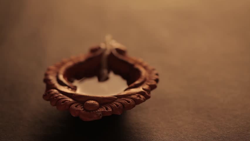 A backlit earthen oil lamp being lit by a male hand during Diwali, creating a warm and festive atmosphere. - Powered by Shutterstock - Get 15% off with code: PIKWIZARD15