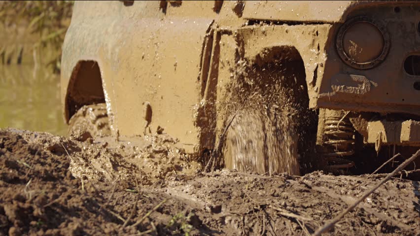 A close-up of the tyre of a muddy SUV slogging through deep mud, splashing water and mud. An SUV stuck in the mud during a race. Slow motion