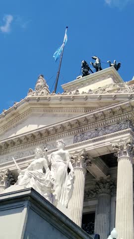 National congress, sculptures, Argentine flag waves at Buenos Aires daylight sky