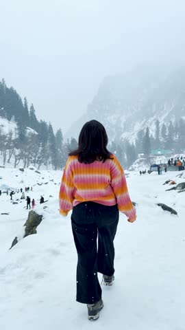 4K Vertical shot of teenager girl raising arms and enjoying snowfall in mountains at Pahalgam, Kashmir, India. Carefree female tourist enjoying holidays during winter. Travel, trekking, active life.
