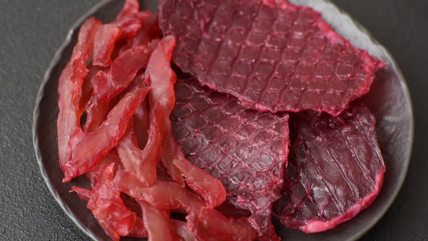 Dried beef slices, jerky, with cherry or plum flavor, salt and spices on a dark concrete background