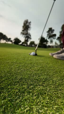 A person is standing on a golf course, holding a golf club and preparing to hit a golf ball