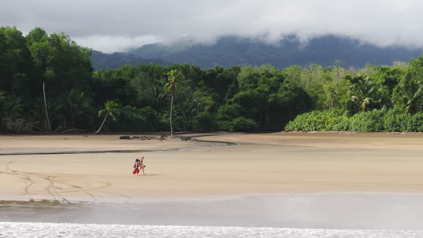 As the sun sets, painting the sky in vibrant colors, two people leisurely stroll along Uvita Beach, captivated by the coastal beauty of Costa Rica