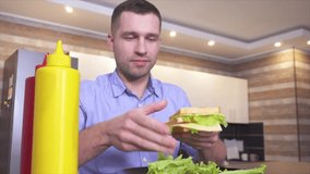 Video of young man sit and eat tasty homemade sandwich. Add some lettuce with mustard and ketchup. Fatning but delicious food. Chewing and biting some more. - Powered by Shutterstock - Get 15% off with code: PIKWIZARD15