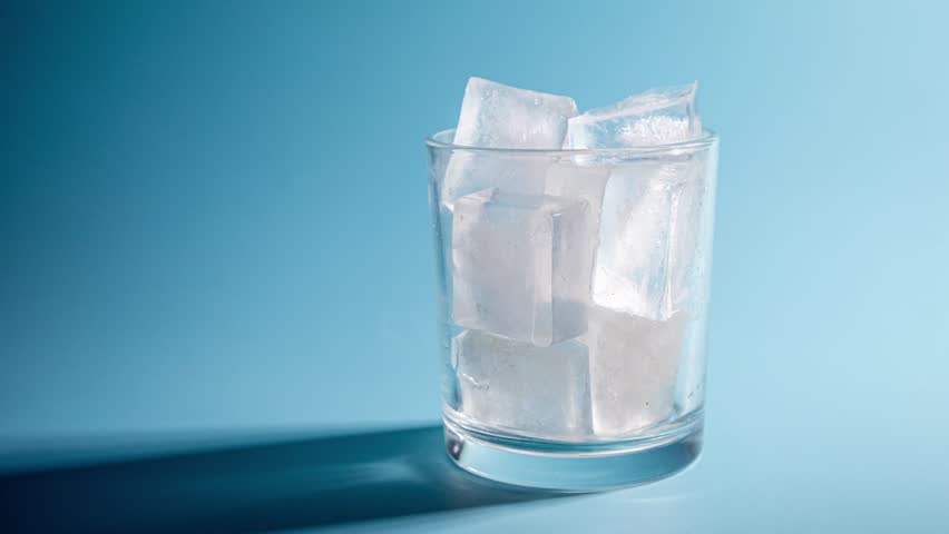 Melting ice cubes in a transparent glass. Timelapse on a blue background.