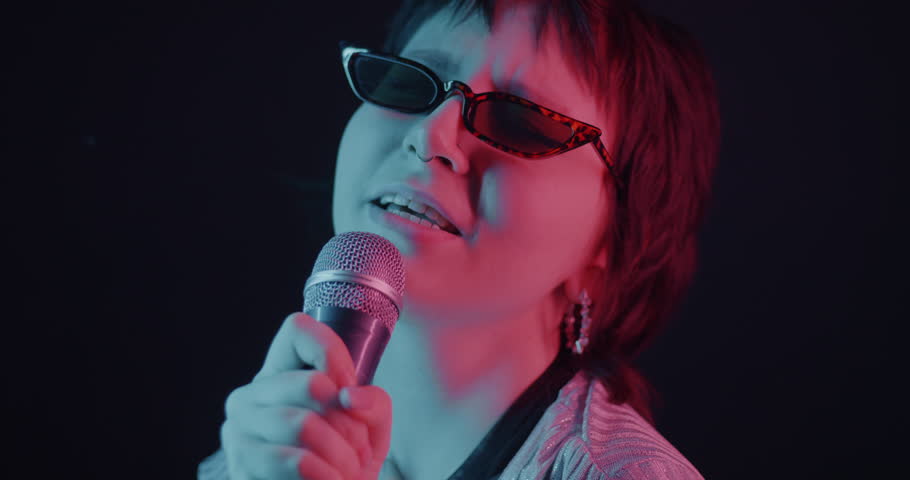 Slow motion of Asian woman singing in microphone dancing in neon light on dark background. Entertainment and youth culture concept.