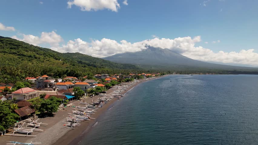 4k drone video of Amed Beach with fishing boats docked on the black sand with a view in the distance of Mount Agung, an active volcano in Amed, Bali Indonesia