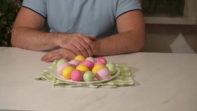 A Caucasian man shows eggs painted with food coloring agents at home in pink, yellow and green colors. A bunch of pastel Easter eggs on a plate. - Powered by Shutterstock - Get 15% off with code: PIKWIZARD15