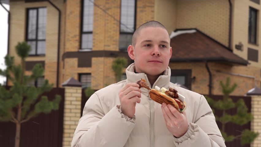 Young man enjoying a delicious hot dog outdoors in winter residential area