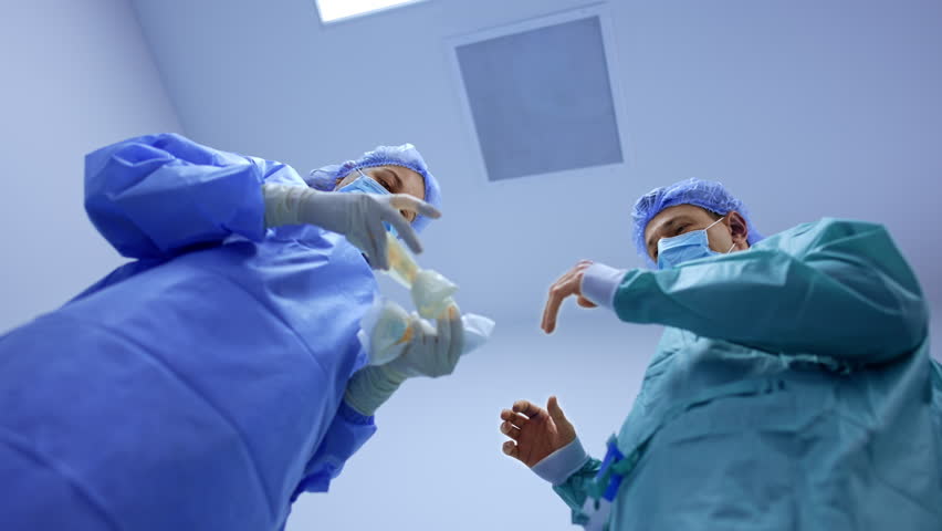 Female nurse prepares latex gloves for the doctor. Male surgeon waiting for the gloves addresses to camera. Low angle view. - Powered by Shutterstock - Get 15% off with code: PIKWIZARD15