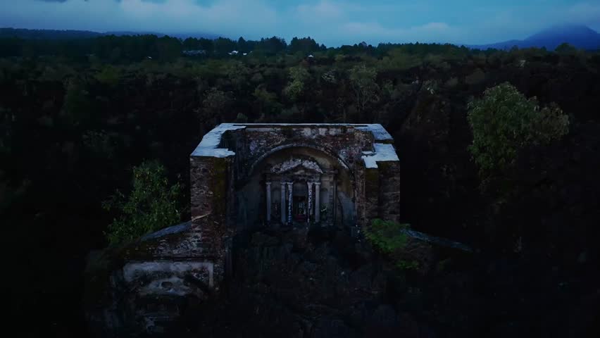 Close-up of altar ruins reveals church facade and bell tower in backward flight. Volcanic eruption site displays cooled lava fields and resilient natural regrowth. San Juan Parangaricutiro, Mexico