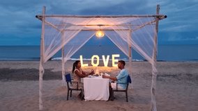 Enjoy an enchanting evening on the beach in Hua Hin, Thailand, where a couple shares a candlelit dinner beneath soft lights, surrounded by serene ocean waves and a beautiful sunset. - Powered by Shutterstock - Get 15% off with code: PIKWIZARD15