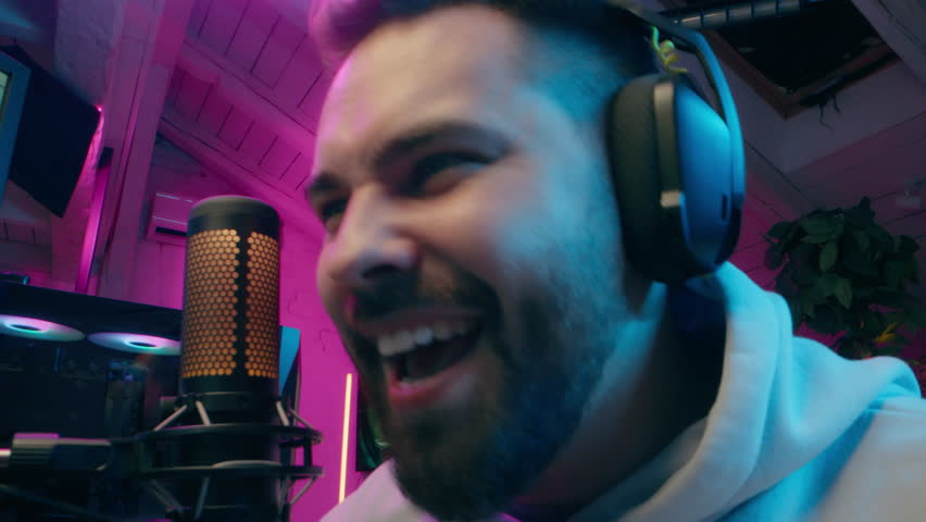 Happy Caucasian guy addict streamer male vlogger man gaming play game tournament computer vlog cyber sport gamer discussing talk microphone tech smiling blogger blogging at home neon influencer stream