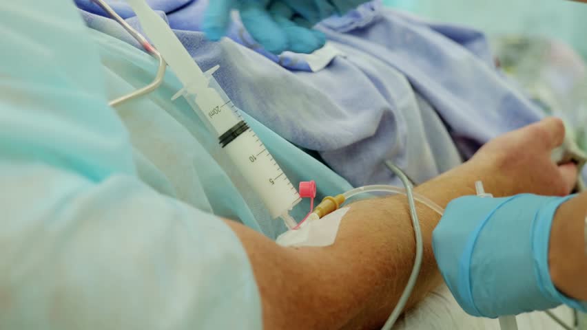 Nurse wearing blue gloves administers medication through an iv catheter in a patient's arm, showcasing a vital healthcare procedure in a hospital environment - Powered by Shutterstock - Get 15% off with code: PIKWIZARD15